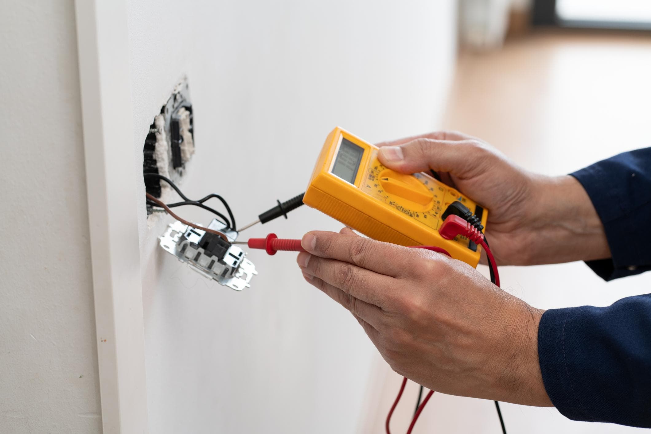 An electrician testing a wall outlet with a multimeter